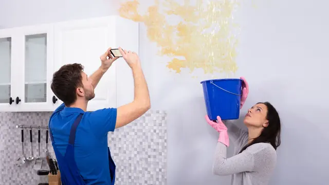 Renter photographing a water-stained wall while another person catches drips in a bucket
