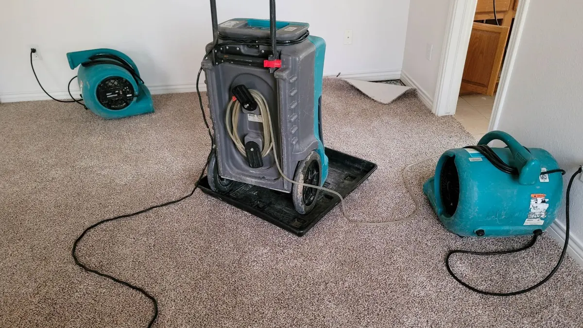 Dehumidifier and two air movers running on carpet during structural drying